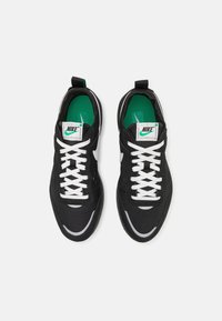 Paire de baskets noires Nike avec lacets blancs et logo swoosh, semelles intérieures vertes et étiquettes de marque blanches vues de dessus sur fond blanc.