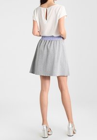 Blusa de color beige claro con abertura en la parte posterior y cinturilla fruncida de color lavanda; falda acampanada gris y zapatos de tacón alto plateados brillantes.