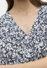 Šaty s květinovým vzorem v námořnické modré a bílé barvě. Mají výstřih do V a lehkou, texturovanou látku.