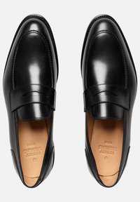 Mocassins en cuir noir avec un bout arrondi, des coutures minimales et une finition lisse. Bride d'accent sur le devant. Détails intérieurs texturés visibles.