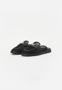 Sorte slip-on sko med mesh-overdel, flad sål og læderdetaljer. Har et guld logo på stroppen.