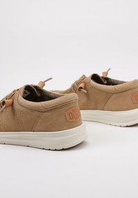 Scarpe in pelle color cuoio con finitura testurizzata, presentano un accento logo di un colore tan chiaro in contrasto e una suola flessibile, progettate per comfort e uso quotidiano.