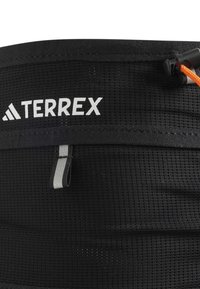Svart Terrex-bånd med et teksturert mesh-design, med en reflekterende grå løkke og en oransje snor for justerbar passform.