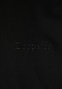Sort stof med en glat tekstur, der har et broderet logo med teksten "Dropsize" i mørk tråd, centralt placeret.