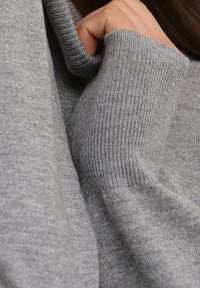 Harmaa neulepusero, jossa ovat resorireunukset hihoissa ja kauluksessa. Kangas näyttää pehmeältä ja teksturoidulta, lähikuvassa näkyvät ompeleet ja taitokset.