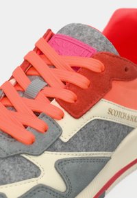 Sneaker med en grå filt-overdel, røde og lyserøde detaljer, orange snørebånd og en struktureret gummisål med branding på siden.