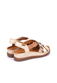 Sandalias de cuero beige y marrón con tiras cruzadas, bordes cosidos y una plantilla acolchada. Suela plana con un acabado texturizado.