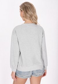 Felpa grigia con maniche lunghe, polsini e orlo a coste, abbinata a pantaloni corti in denim azzurro. Il materiale sembra morbido e confortevole.