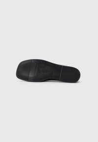 Suola di scarpa in gomma nera con scanalature orizzontali e verticali, caratterizzata da dettagli del brand in rilievo e un design piatto per una migliore aderenza.