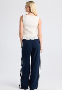 Cream-colored smocked top with a ruffled hem, paired with navy wide-leg pants featuring white side stripes. Smooth texture, casual design.