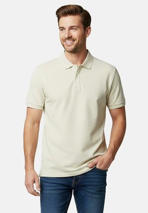 Lichtbeige poloshirt met kraag en korte mouwen, voorzien van een subtiele textuur, een aansluitend ontwerp en een enkele knoopsluiting. Draagt blauw spijkerbroek.