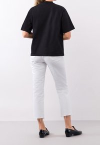 Svart kortärmad t-shirt med rund hals, i kombination med beskurna vita jeans och svarta slip-on-skor, sedd bakifrån.