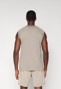 Αμάνικο αθλητικό τοπ σε ανοιχτό μπεζ χρώμα, κατασκευασμένο από λείο ύφασμα. Διαθέτει στρογγυλή λαιμόκοψη και διακριτικό λογότυπο στο πίσω μέρος. Συνδυάζεται με σορτς στο ίδιο χρώμα.