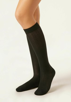 Chaussettes noires montantes en tissu texturé avec un motif géométrique. Elles présentent une finition côtelée et lisse.