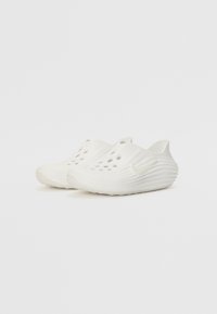 Zoccoli bianchi senza lacci con fori aperti per ventilazione, texture ribbata e un sottile accento con logo a contrasto sul lato.