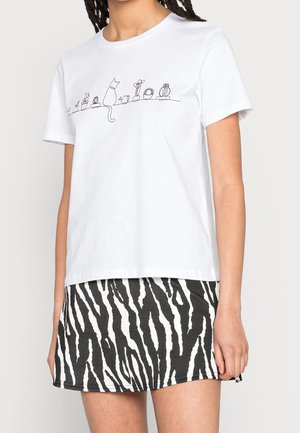 Weißes Baumwoll-T-Shirt mit kurzen Ärmeln, das eine minimalistische Linzeichnung einer Katze und Kakteen über die Brust zeigt. Kombiniert mit einem Rock im Zebradruck.