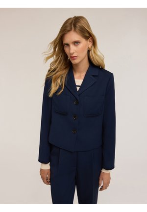 Blazer corto en navy de tejido texturizado con dos bolsillos frontales, tres botones negros y un cuello con muesca. Estilizado con una camiseta de rayas por debajo.