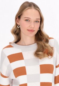 Strickpullover mit einem Farbblockdesign in Orange, Grau und Creme. Weiche Textur mit einem gerippten Ausschnitt und langen Ärmeln.