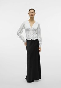 Blusa de satén blanco con escote en V profundo y cierre de botones, combinada con una falda larga negra, que presenta una textura suave y una silueta elegante.