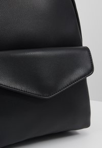 Černý kožený batoh s texturovaným povrchem, s překlopným uzávěrem a elegantními liniemi. Hladké akcenty zvýrazňují design.