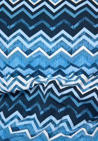 Stoff mit Chevron-Muster in unterschiedlichen Blau-, Marine- und Weißtönen. Das Design umfasst abwechselnde Streifen und hat eine strukturierte Optik.