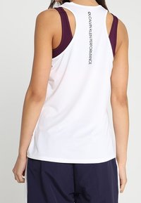 Camiseta atlética blanca con diseño de espalda de nadador, tirantes morados contrastantes y texto en negro "CALVIN KLEIN PERFORMANCE" en la parte posterior.