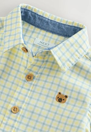 Sárga és kék kockás ing farmergallérral, fából készült gombokkal és a mellrészen barna hímzett medvével.