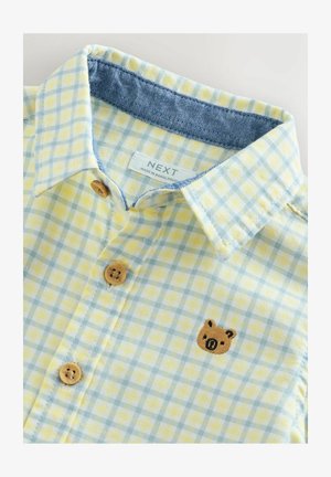 Sárga és kék kockás ing farmergallérral, fából készült gombokkal és a mellrészen barna hímzett medvével.