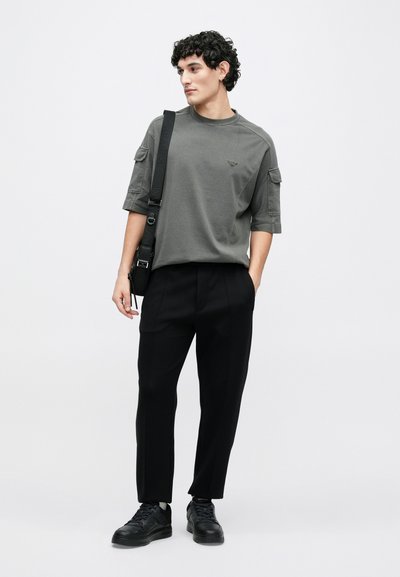 Šedé bavlněné tričko s krátkými rukávy a bočními kapsami. Doplněno černými kalhotami na míru a černými teniskami pro vyvážený vzhled.