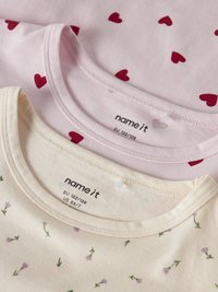 Deux chemises pour enfants pliées, taille UE 122/128 ; une rose clair avec des cœurs rouges, l'autre crème avec de petites fleurs violettes.