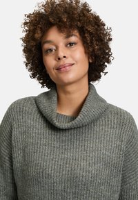 Grau gestrickter Pullover mit weitem, gerolltem Ausschnitt, gerippter Textur und lockerer Passform, ausgestattet mit langen Ärmeln und weichem Stoff.