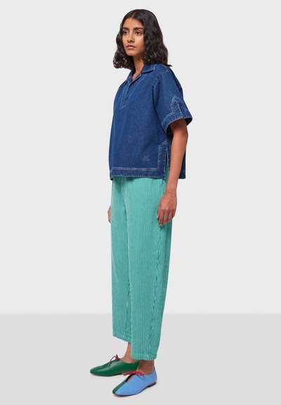 Camicia di jeans oversize blu; pantaloni a gamba larga verde con strisce verticali; scarpe bicolore: verdi e blu con dettagli rossi.