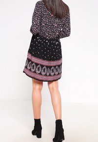 Vestido negro con parte superior floral, acentos en rosa y dobladillo estampado. Tiene mangas largas y una falda acampanada. Se lleva con botas negras hasta el tobillo.