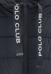 Giacca a vento blu navy con chiusura a zip, caratterizzata da sezioni trapuntate verticali e zip con tiranti contrassegnati con il testo "POLO CLUB" in bianco.