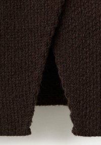 Nahaufnahme von dunkelbraunem grob gestricktem Stoff mit sichtbarer dicker Garnstruktur und Rippenmuster am Rand.