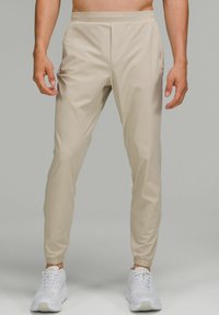 Beiga träningsbyxor med en slät textur, avsmalnande passform och elastisk midja. Har sidofickor och ankle cuffs. Bärs med vita sneakers.