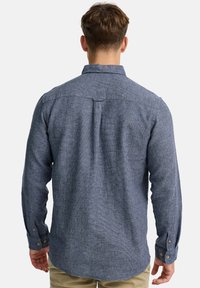 Camisa de hombre de manga larga en una tela azul texturizada. Presenta un cuello abotonado, puños ajustables y un dobladillo curvado para un ajuste moderno.