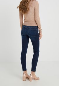 Mörkblå skinny jeans med två bakfickor, matchade med en ljusrosa, skimrande åtsittande tröja och beige klacksandaler.
