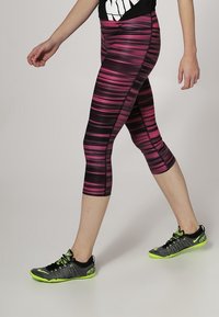 Leggings capri a righe rosa e nere con una vestibilità comoda, abbinati a scarpe da ginnastica nere e verde neon. Tessuto texturizzato, design elegante.