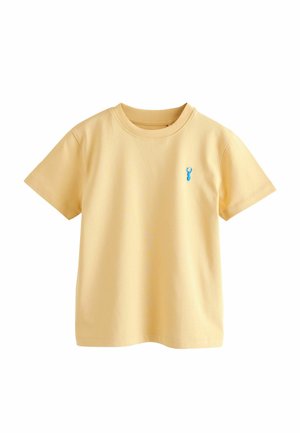 Jasnożółty t-shirt z krótkim rękawem i okrągłym dekoltem, z małym niebieskim emblematem jelenia na lewej piersi, prezentowany na białym tle.