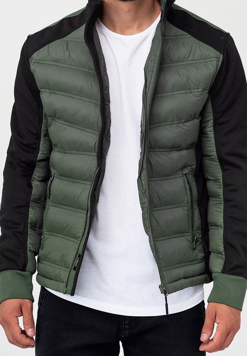 Zielono-czarna kurtka puchowa z suwakiem z przodu, z poziomymi pikowanymi sekcjami i ściągaczami przy mankietach. Gładki, lekki materiał.