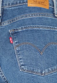 Džínové kalhoty s výjimečným designem zadní kapsy s křivým švem, světle modré barvy a červenou značkou Levi's u kapsy.