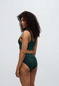 Σκούρο πράσινο ριμπ crop top και σλιπ ψηλόμεσο με αντίθετη ανοιχτή ραφή. Ομαλή υφή και αθλητικός σχεδιασμός, εφαρμοστή σιλουέτα.