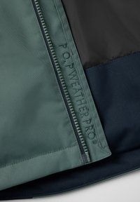 Groene regenjas met een navy voering, ritsluiting en ingegraveerde "P.O.P WEATHERPRO" tekst op de stof. Zachte textuur.