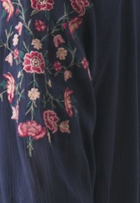 Marinblus med intrikata blommönster i rosa, rött och grönt. Texturerad tyg med en mjuk, flödande design.