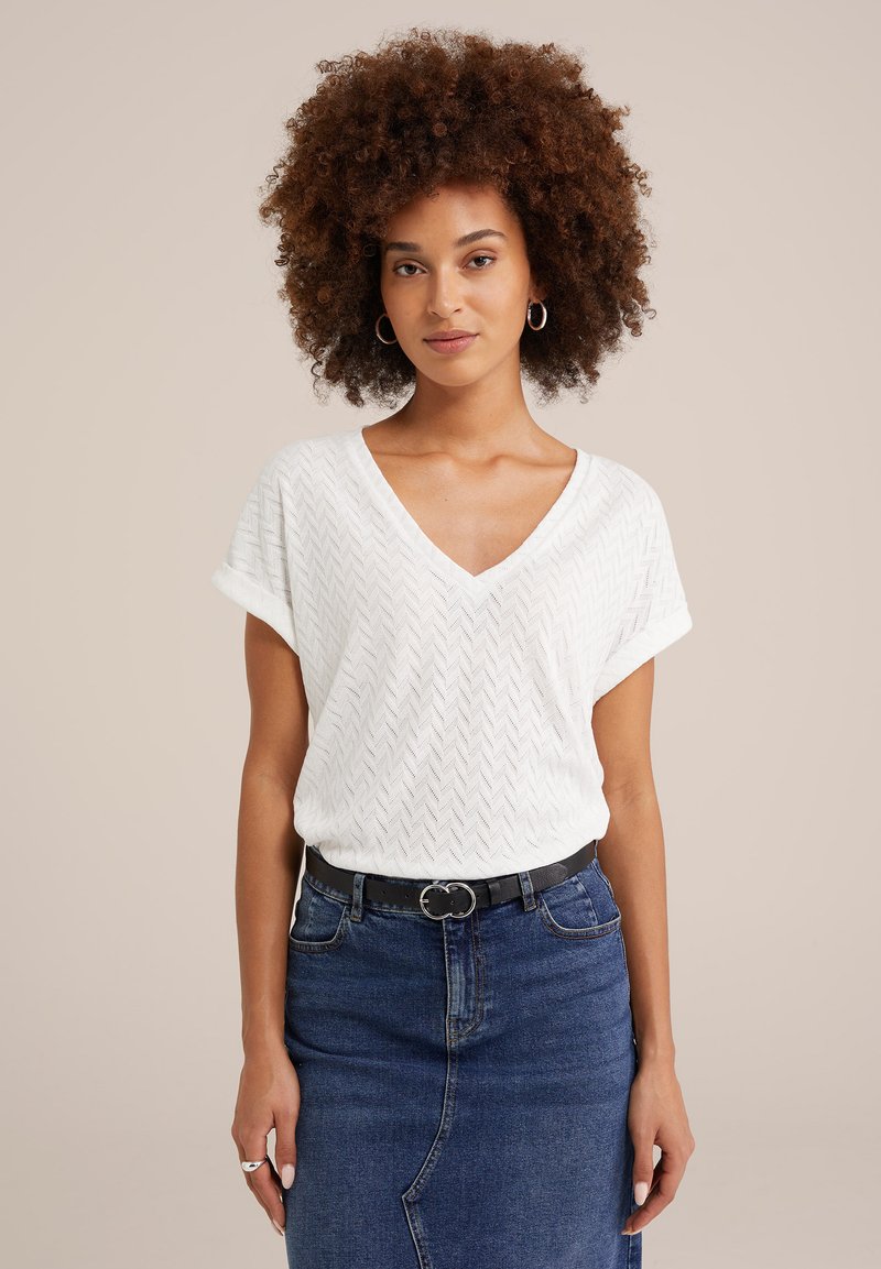 Top bianco a maglia con scollo a V e maniche corte arrotolate, abbinato a una gonna di jeans blu e a una cintura nera con fibbia argentata.