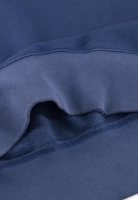 Felpa blu navy con una texture liscia e polsini a costine. Dettaglio notevole include una cucitura a contrasto lungo l'orlo.