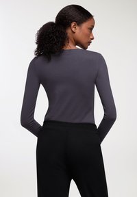 Maglietta a maniche lunghe grigia realizzata in tessuto liscio, abbinata a pantaloni neri con vita elastica. Design semplice, senza motivi o dettagli.