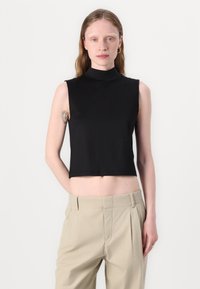Musta, hihaton mock neck lyhyt toppi sileässä kankaassa. Huomattava yksityiskohta: istuva siluetti. Yhdistetty vaaleanbeigeihin korkeavyötäröisiin housuihin.