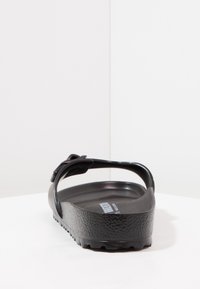 Sandal negru din plastic cu un călcâi texturat, curea ajustabilă și talpă conturată. Design deschis care permite circulația aerului.
